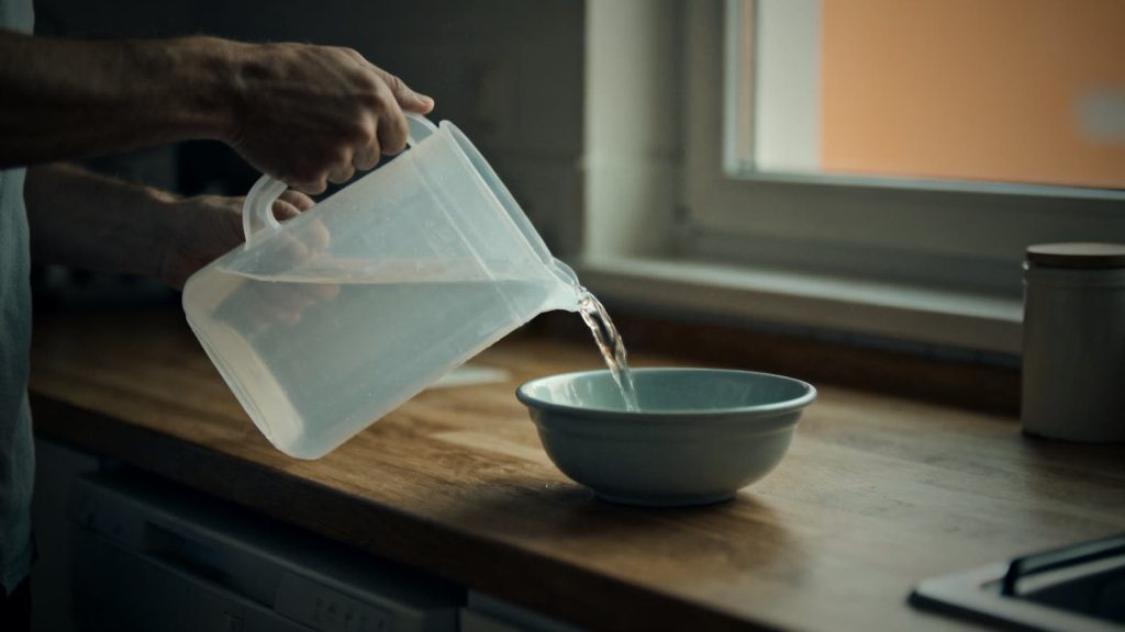 Manos vertiendo agua de una garrafa en un barreño para lavarse las manos con poca agua y sin agua corriente