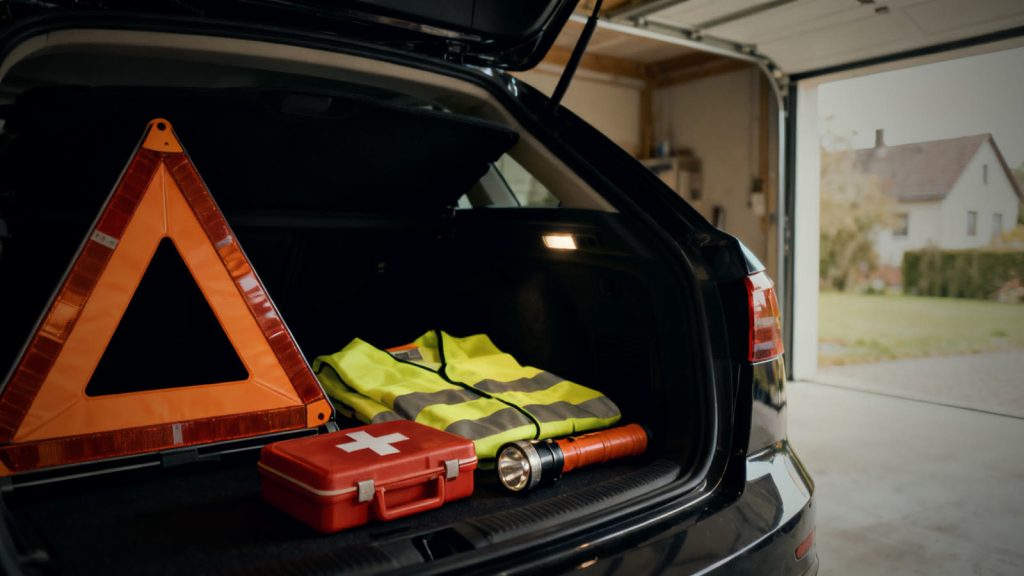 Geöffneter Kofferraum mit Warndreieck, Warnweste und Verbandskasten als Notfallausrüstung fürs Auto