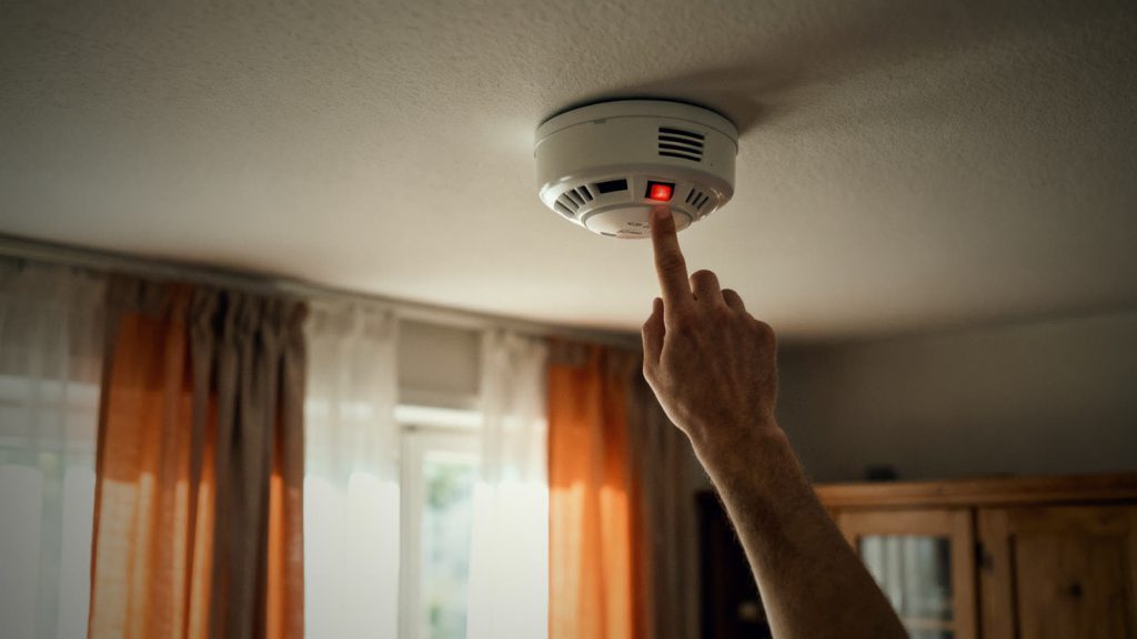 Una mano prueba un detector de humo en el techo de un salón, símbolo de la protección contra incendios en el día a día
