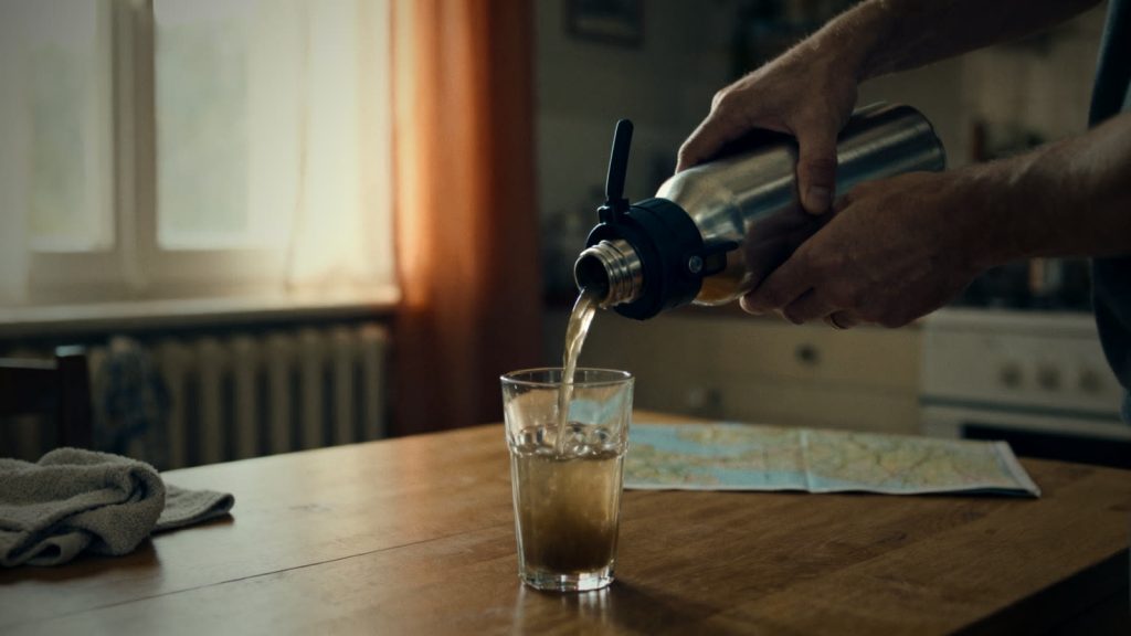 Hände filtern trübes Wasser mit einem tragbaren Wasserfilter in ein Glas auf einem Holztisch