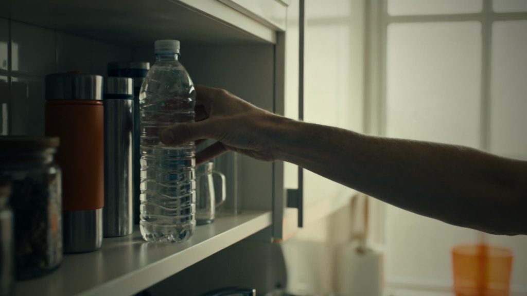 Eine Hand stellt eine Wasserflasche ins Regal als Teil eines einfachen Notvorrats